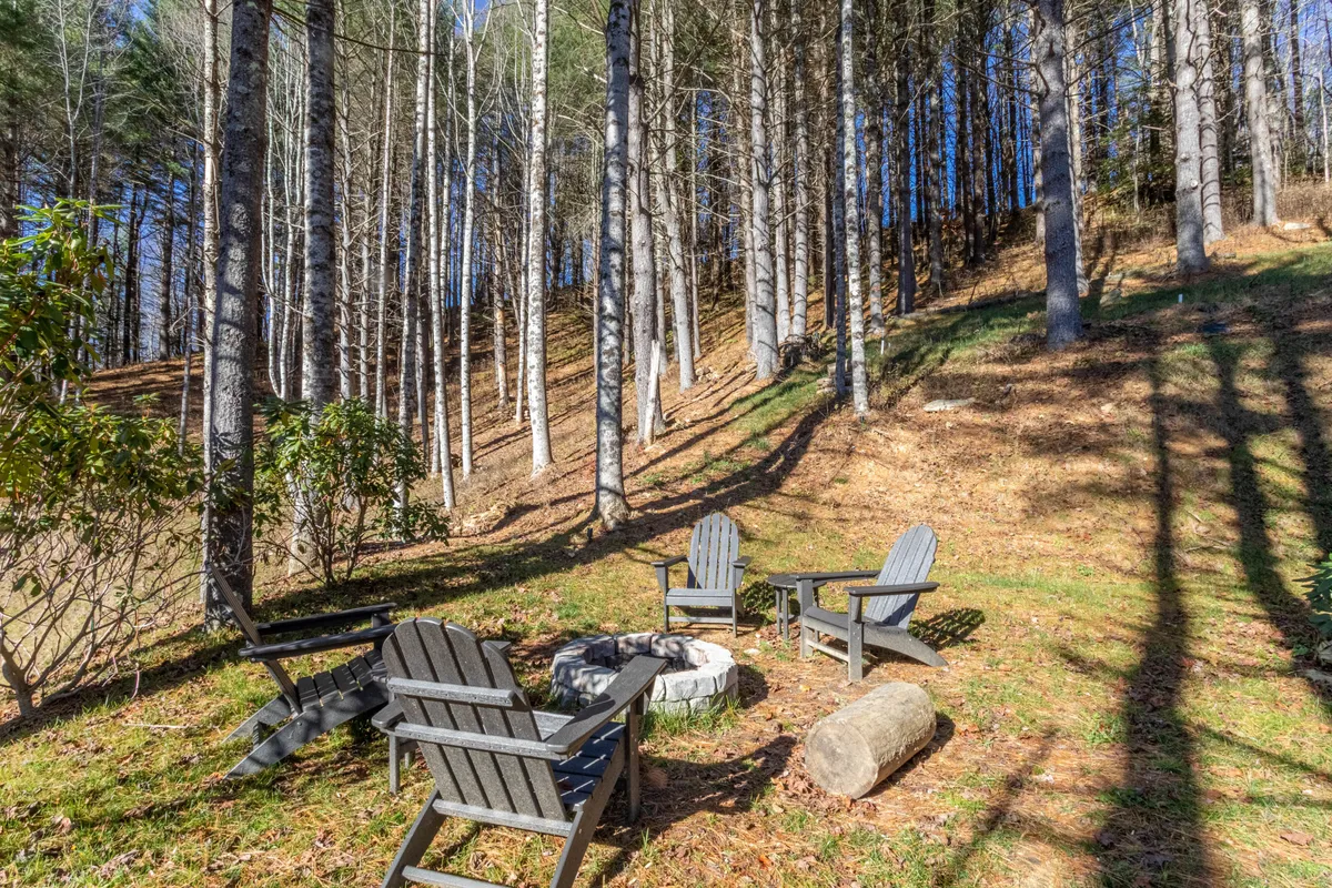 A cozy fire pit area set among tall trees, surrounded by Adirondack chairs. The scene is perfect for stargazing, storytelling, and enjoying memorable evenings under the open sky, with a natural backdrop highlighting the outdoor living experience.