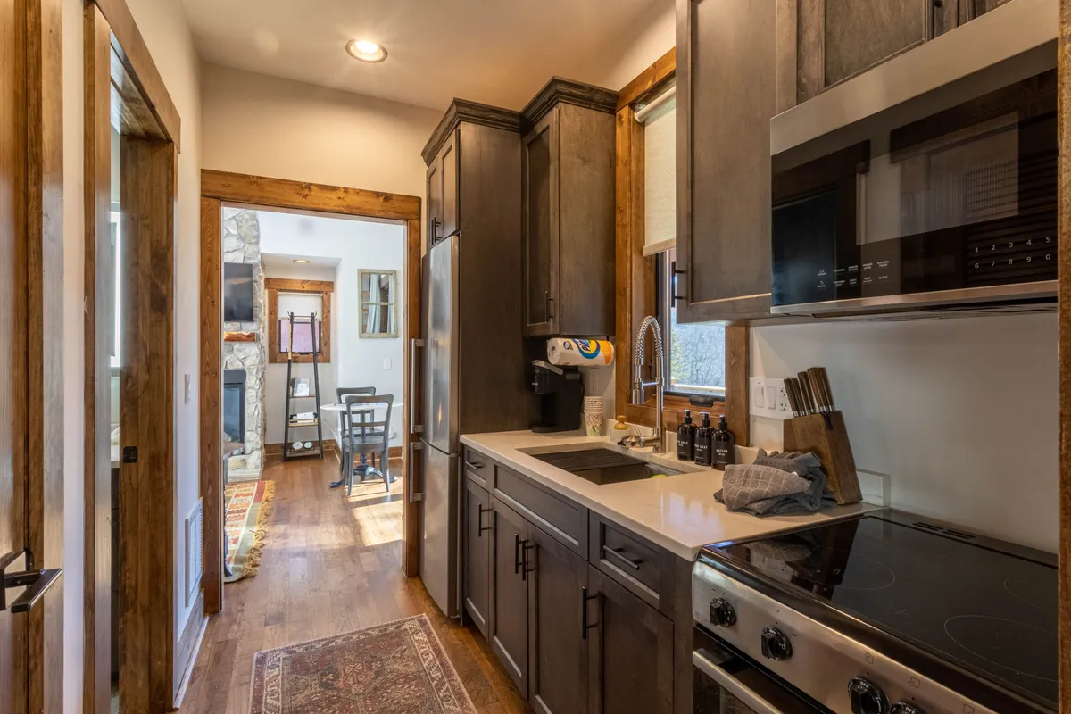 A warmly lit kitchen showcases sleek cabinetry, stainless steel appliances, and a bright window view. Counters display a variety of utensils and cookware, suggesting readiness for both elaborate meals and casual breakfasts. The open layout invites interaction, hinting at seamless transitions from cooking to dining.