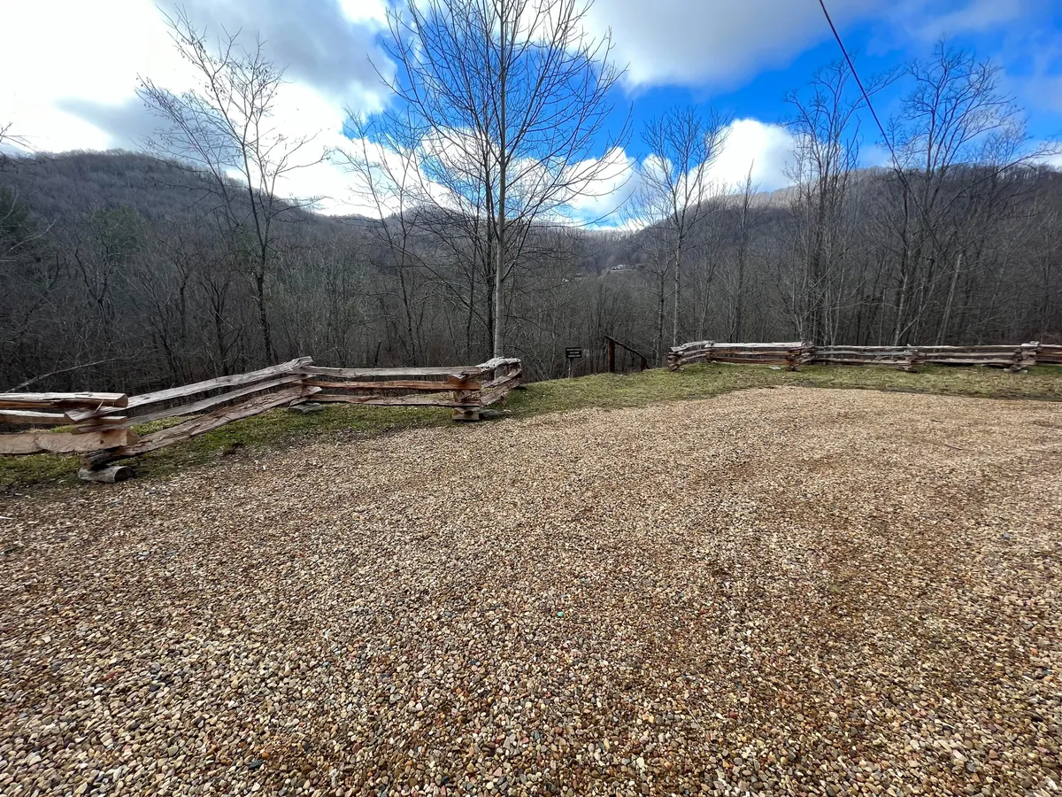This image captures a tranquil exterior setting with a gravel clearing, bordered by a wooden fence, and framed by distant mountains and bare trees. The open area invites outdoor gatherings, contemplative nature walks, or peaceful stargazing, all under the calming influence of sunset lighting. Wildlife sightings and the hush of solitude are suggested by the untouched natural landscape.