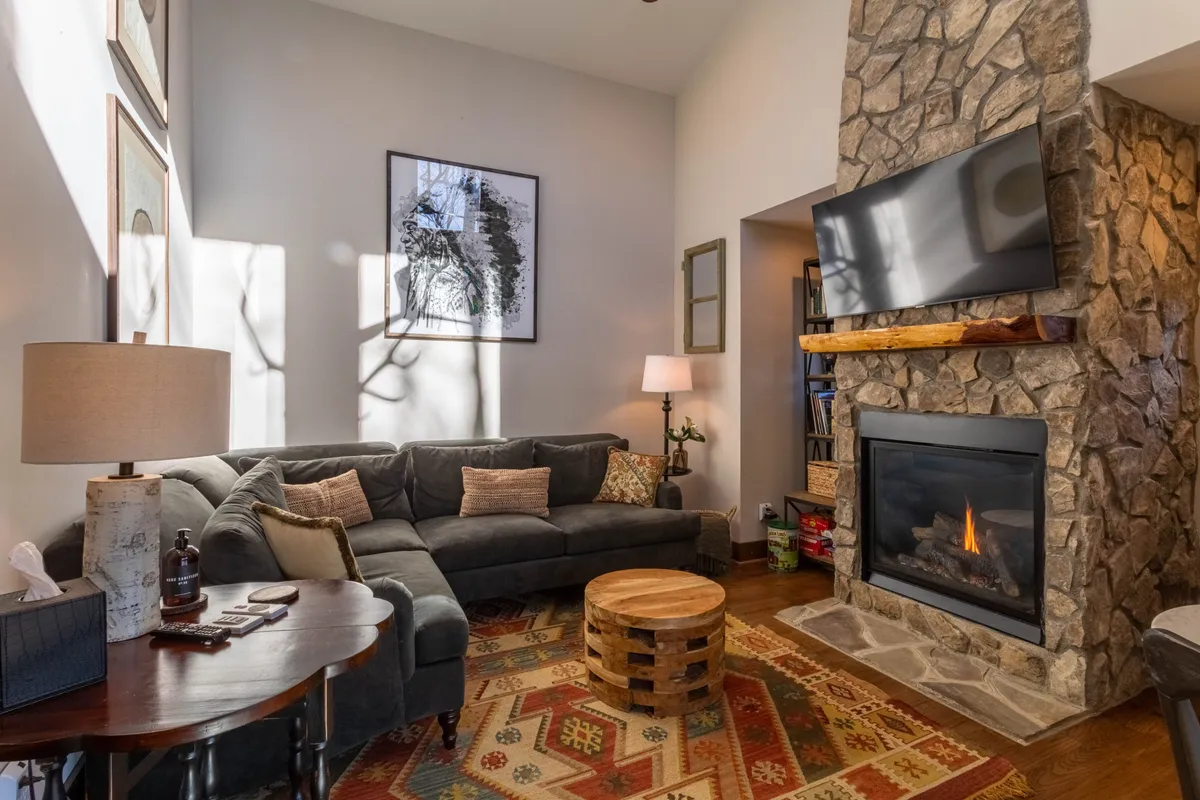 A warmly lit living room featuring a prominent stone gas fireplace, a plush sofa facing a coffee table, and tasteful artwork adorning the wall. The arrangement offers a cozy atmosphere perfect for relaxing, entertaining, or enjoying a movie night.