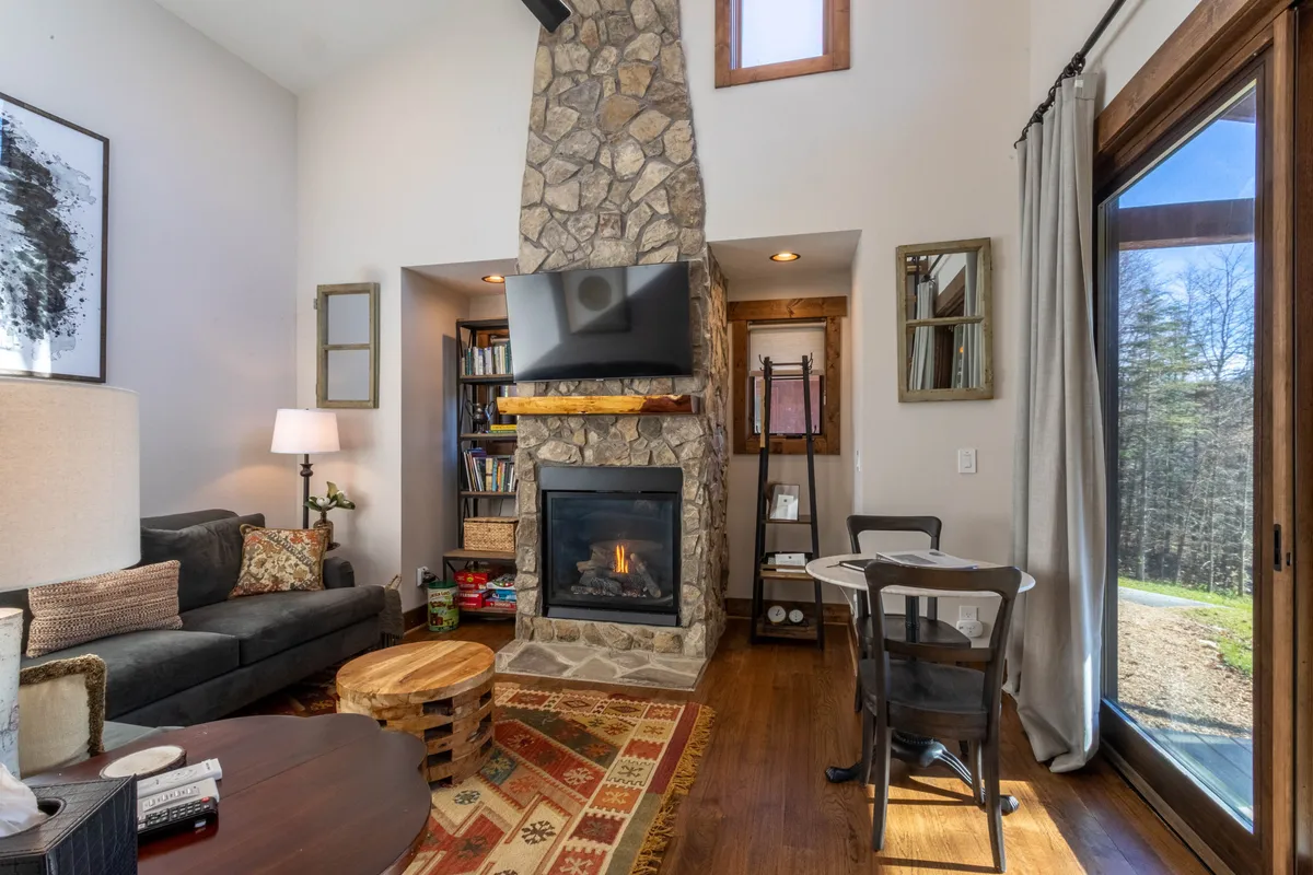 An inviting living and dining area with a stone fireplace, a large, comfortable sofa, a dining table, and expansive windows that let in natural light. The setting is styled for both relaxation and social interaction, emphasizing warmth and togetherness.