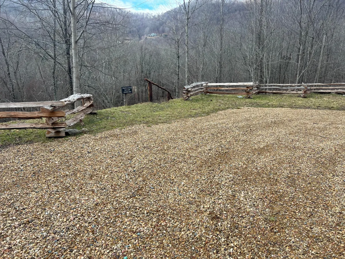 A broad view of a gravel area edged by wooden fencing, with a tree line and mountains rising in the distance. The open space invites guests to envision outdoor gatherings, picnics, or watching sunsets over the mountains.